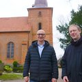 Zwei Männer in schwarzen Jacken stehen vor einer Kirche