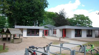 Eingangsbereich im Hintergrund, links ein Holzhäuschen, rechts im Vordergrund Fahrradständer