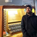 Ein Mann sitzt mit Mütze und Jacke vor einer beleuchteten Orgel