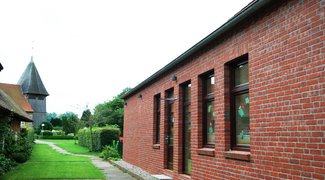 Rechts im Bild die Fassade der Kita mit geschmückten Fenstern, hinten links der Kirchturm