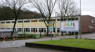 Blick aufs gelbe Gebäude von außen, im Vordergrund Hinweisschilder